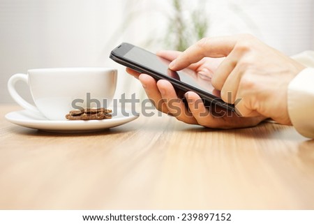 man is using mobile smart phone near cup of coffee