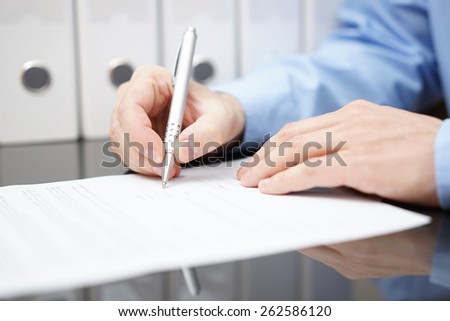 Closeup of businessman is signing contract with documentation in background