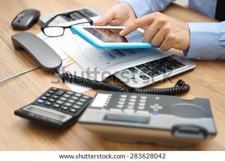 busy businessman  in office with full of accessories on desk with telephone handset off the hook and working on tablet computer