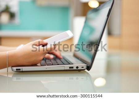busy young woman is typing on laptop computer and using mobile phone at the same time