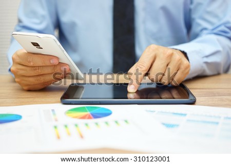 busy businessman  with financial documents working in office with tablet computer and smart phone at the same time