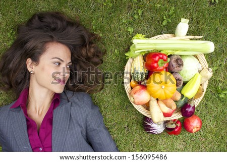 happy corporate woman lying on grass next to vegetable basket