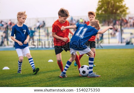 Kids Kicking Football Ball. Boys Play Soccer on Grass Field. Spectators Parents in the Background. Youth Players kicking Soccer Match on grass Stadium. Youth Football Tournament