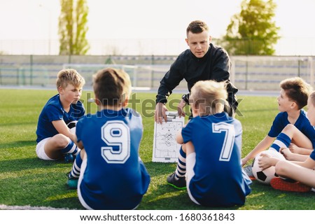 Young coach teaching kids on football field. Football coach coaching children. Soccer football training session for children. Football tactic education. Coach explains a game strategy using board