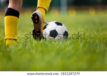 Closeup of soccer player running and kicking soccer ball on grass lawn. Legs of footballer playing competition match. Sports horiznotal background. Athlete in soccer cleats and soccer socks