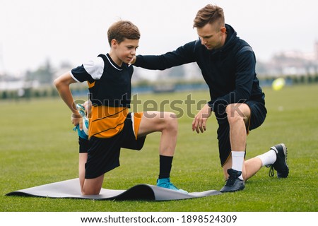 Soccer Coach With Young Player. Boy on Football Field Stretching on Exercise Mat. Male Coach and Personal Trainer Giving Advices to Young Athlete