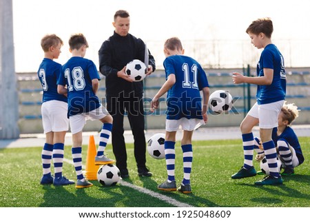 Young coach teaching kids on football field. Trainer explains to schoolboys training rules. Football coach coaching children. Soccer football training session for children. Football tactic education. 