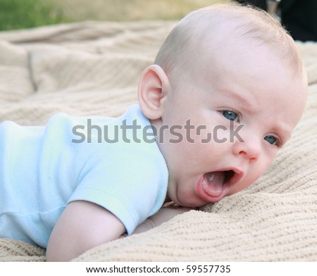 Open mouthed baby boy with blue eyes on tummy tries to learn to crawl