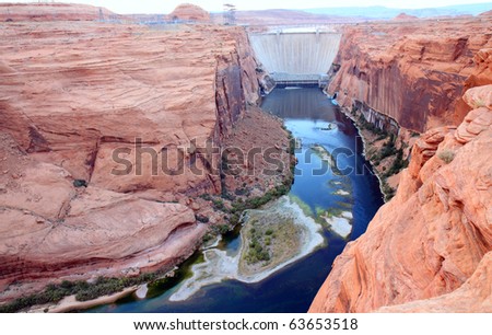 Glen canyon dam harnesses electricity from the Colorado River and forms the border of Lake Powell.  Tall, sheer, orange colored canyon walls tower over the river, forming great viewpoints