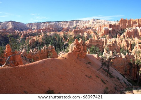 Hiking trails wind through luminous orange sandstone spires, sculpted by wind and water erosion, towering above Bryce canyon\'s valley floor