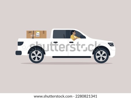 A young driver of a pickup truck driving with one elbow hanging out of the window, a cardboard box in the trunk