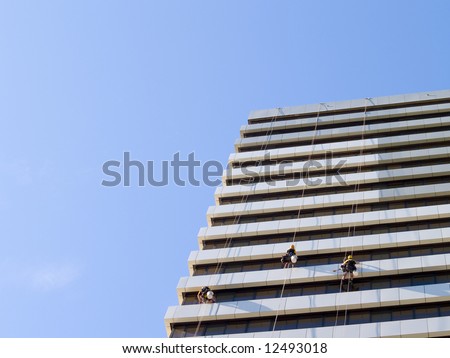 abseiling window cleaners series -  3 window cleaners dangling  with large blue sky to the left