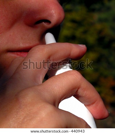 Specific hand attitude using a puffers device to deliver medication into the nose.The background can suggest the source of allergy(the plants)