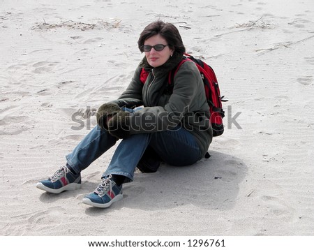 A girl sitting in the sand on the ocean beach in a very cold and windy winter day