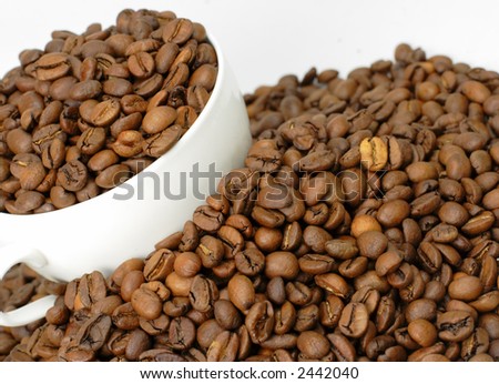 A cup of coffee full with coffee beans in the middle of a heap of coffee beans stacks.