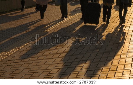 Image of travellers shadows on a pavement road in a dusk city.