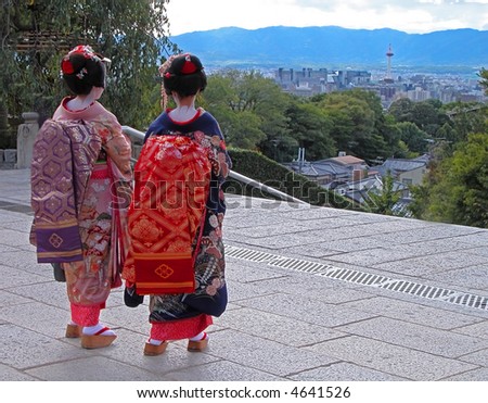 A very specific travel image for Kyoto,Japan:two geishas in front of Kyomizudera temple looking to the city with Kyoto Station tower visible in the distance.