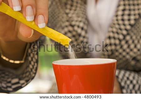Close-up image of a woman hand putting sugar in a red cup of coffee