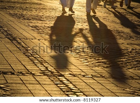 Soft aspect of the shadows of a couple hand in hand walking in a pavement square in the dusk lighting.