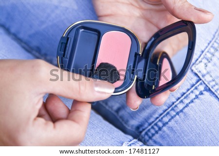 Woman\'s hands holding a makeup kit and a brush over her thighs while wearing jeans.