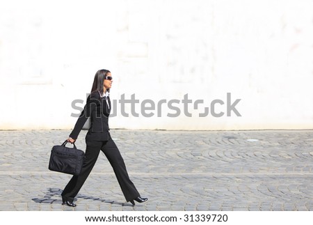 Young businesswoman walking along a cobbled street in front of a white wall.