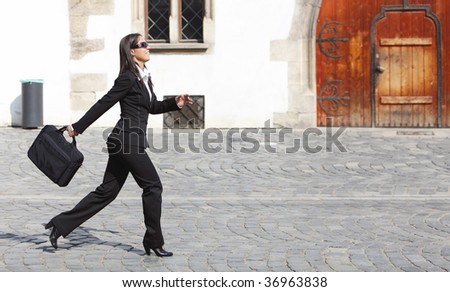 Young businesswoman walking along a cobbled street in front of an old building wall.