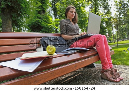 Young woman studying outside in a park on a bench.The focus is selective on the bitten apple.