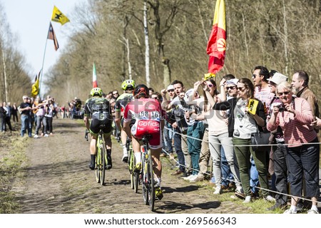 TROUEE d\'ARENBERG, FRANCE- APR 12: Group of three cyclists pedaling in front excited spectators on the famous cobblestone road from the forest of Arenberg during the Paris Roubaix 2015 race.