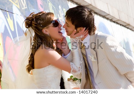 Pretty bride kissing groom at graffiti wall background