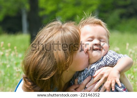 Happy mother kissing little son at summer park