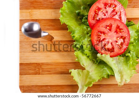 Red tomato slices, salad leaves and a knife on chopping board