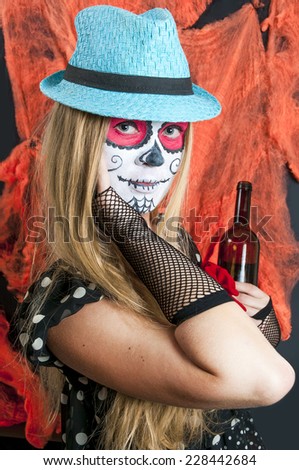 Portrait of pretty young girl with Calavera Mexicana makeup mask in the blue hat. Halloween party