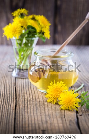 Flower honey in a glass jar and dandelions on a wooden table