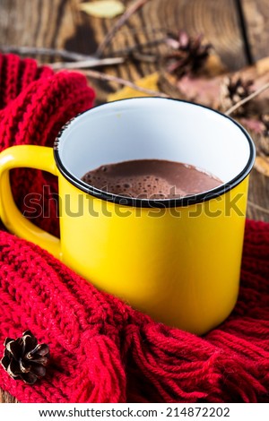 Mug full of hot chocolate on a knitted woolen scarf. Warming drink for fall and winter