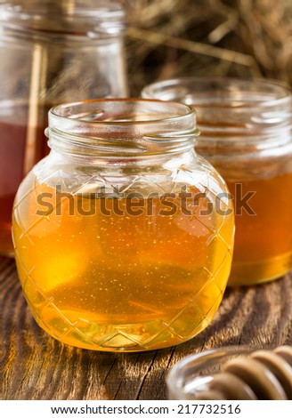 Different varieties of organic raw honey in a glass jar on a wooden rustic background