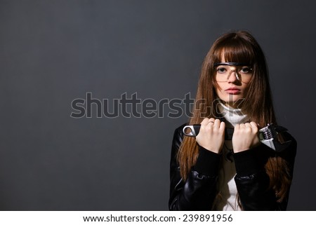 Girl in safety glasses with adjustable wrench on a dark background
