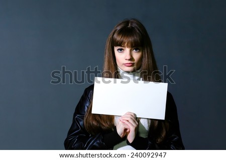 Girl with empty white blank card on a dark wall background