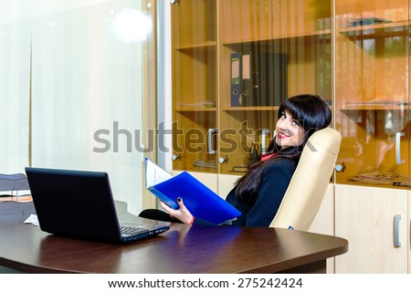 Smiling beautiful businesswomen sitting at the table in the office with paperwork and laptop