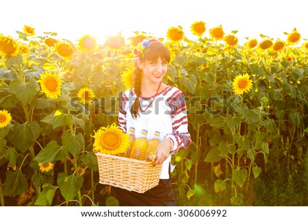 Smiling woman in embroidery holding a basket with sunflower oil on a field