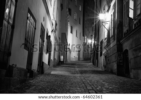A black and white of a dark European alleyway at night in horizontal