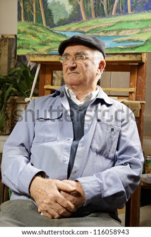 Artist sitting in chair under his painting looking sideways