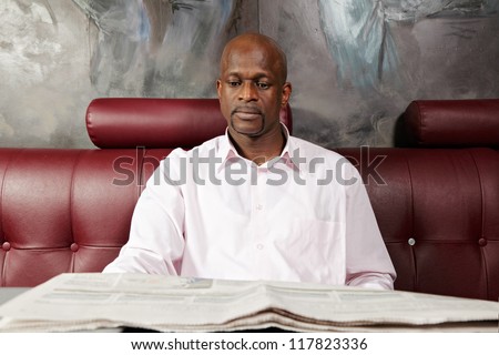 African man reading paper while sitting on red leather sofa