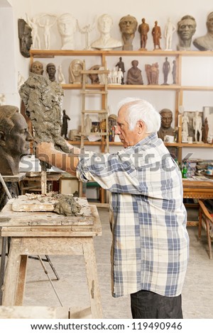 Senior sculptor making sculpture putting clay on wire skeleton profile view