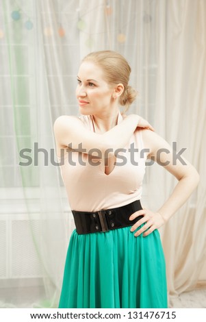 Young blonde dancer wearing green skirt standing in static pose and looking sideways