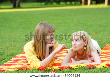 Young woman proposing cherry to friend both laying in meadow