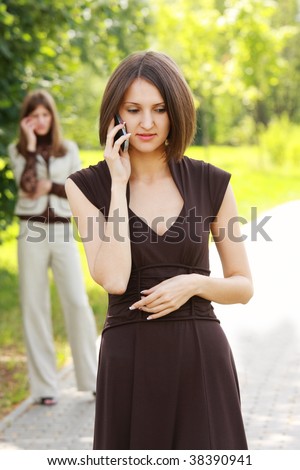 Two young women talks on phone outdoors selective focus
