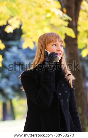 Young blond woman walks in autumn park and talks on phone