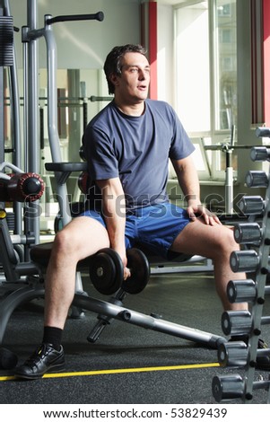 Man in shirt and shorts at gym with dumb-bell looking sideways