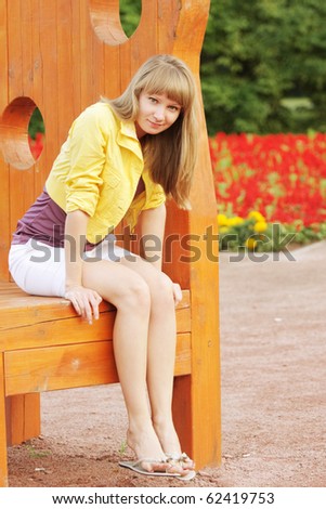 Young blonde woman sitting on big wooden stool in park