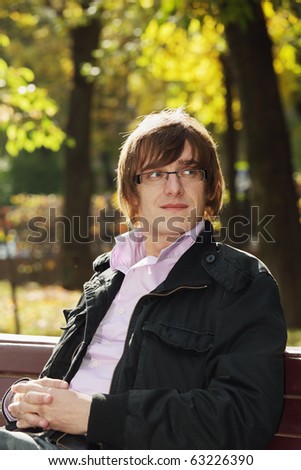 Young man wearing casual clothes sitting in park on bench
